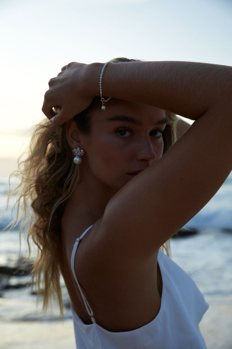 Charming Rose Gold Pearl Bracelet - Enhancing Your Bridal Look with Subtle Elegance. Worn on a blonde model on the beach holding her hair up and away from her face.