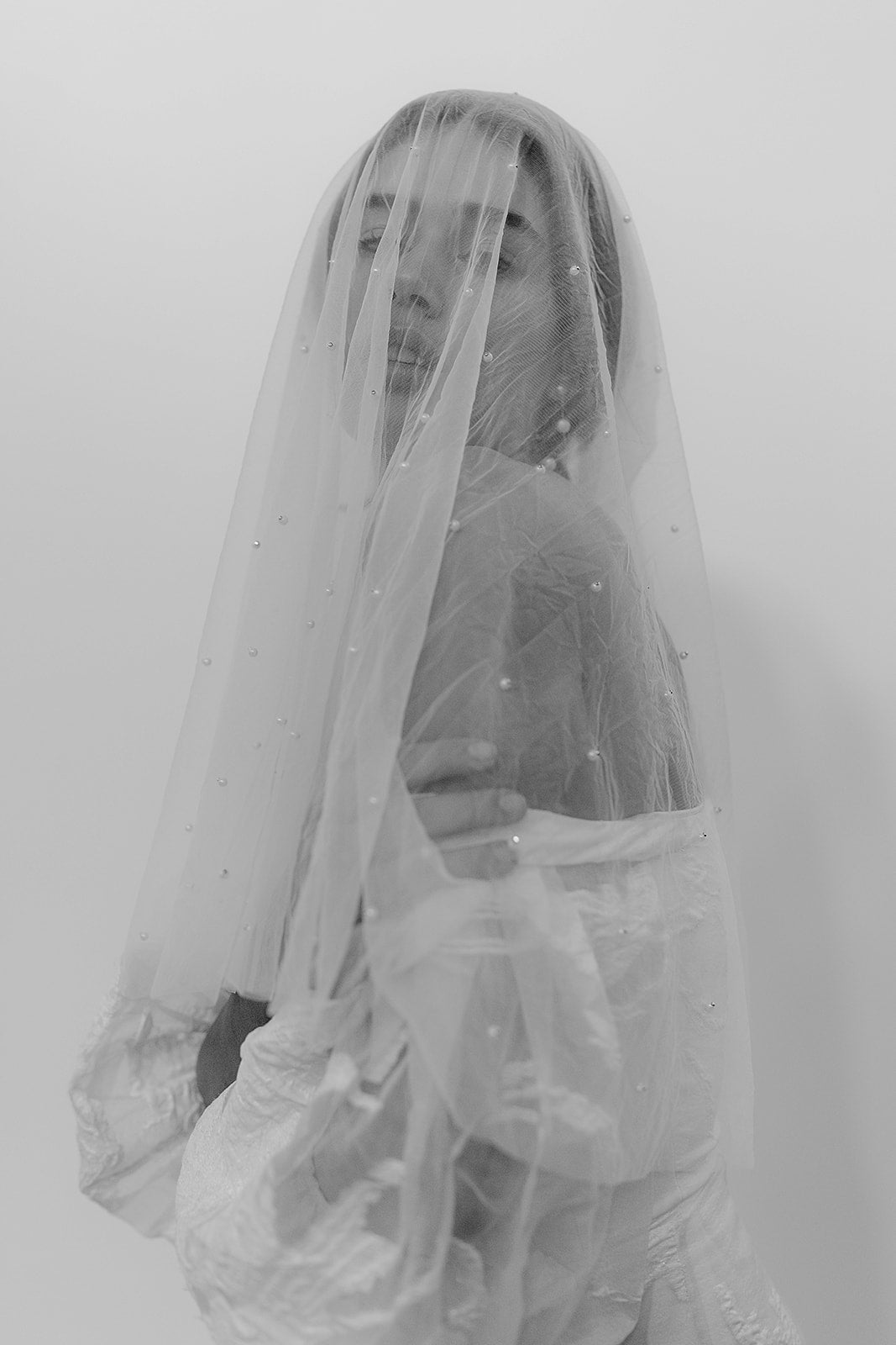 Classic pearl wedding veil with blusher over face worn by a bride, adding elegance to her bridal ensemble.