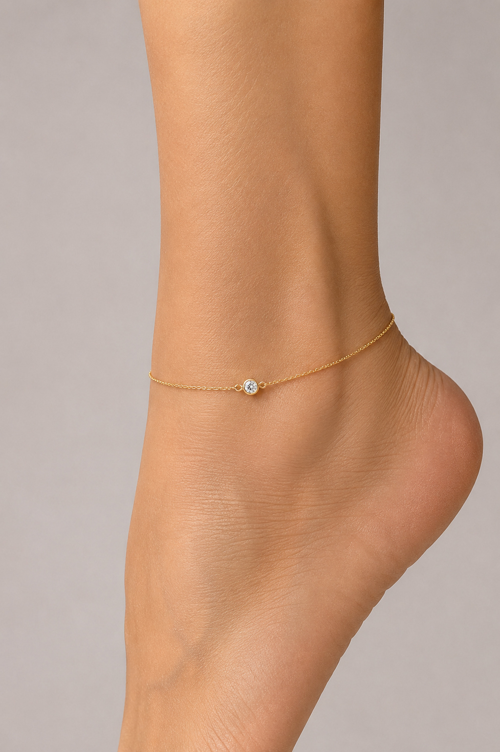 Gold anklet with a small gemstone on a foot against a neutral background