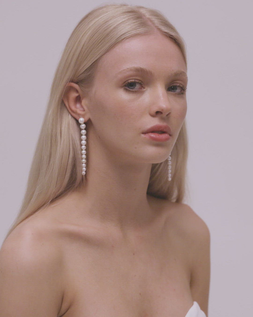 Video of a blonde bride with natural straight hair style and middle part showing pearl string earrings.