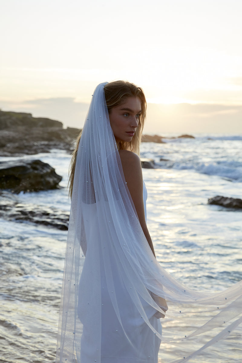 Elegant Pearl Wedding Veil by Amelie George Bridal on a beach bride looking out to the ocean.