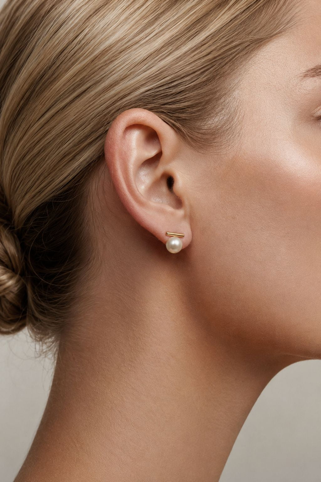 Close-up of a woman wearing pearl wedding earrings with a neutral background