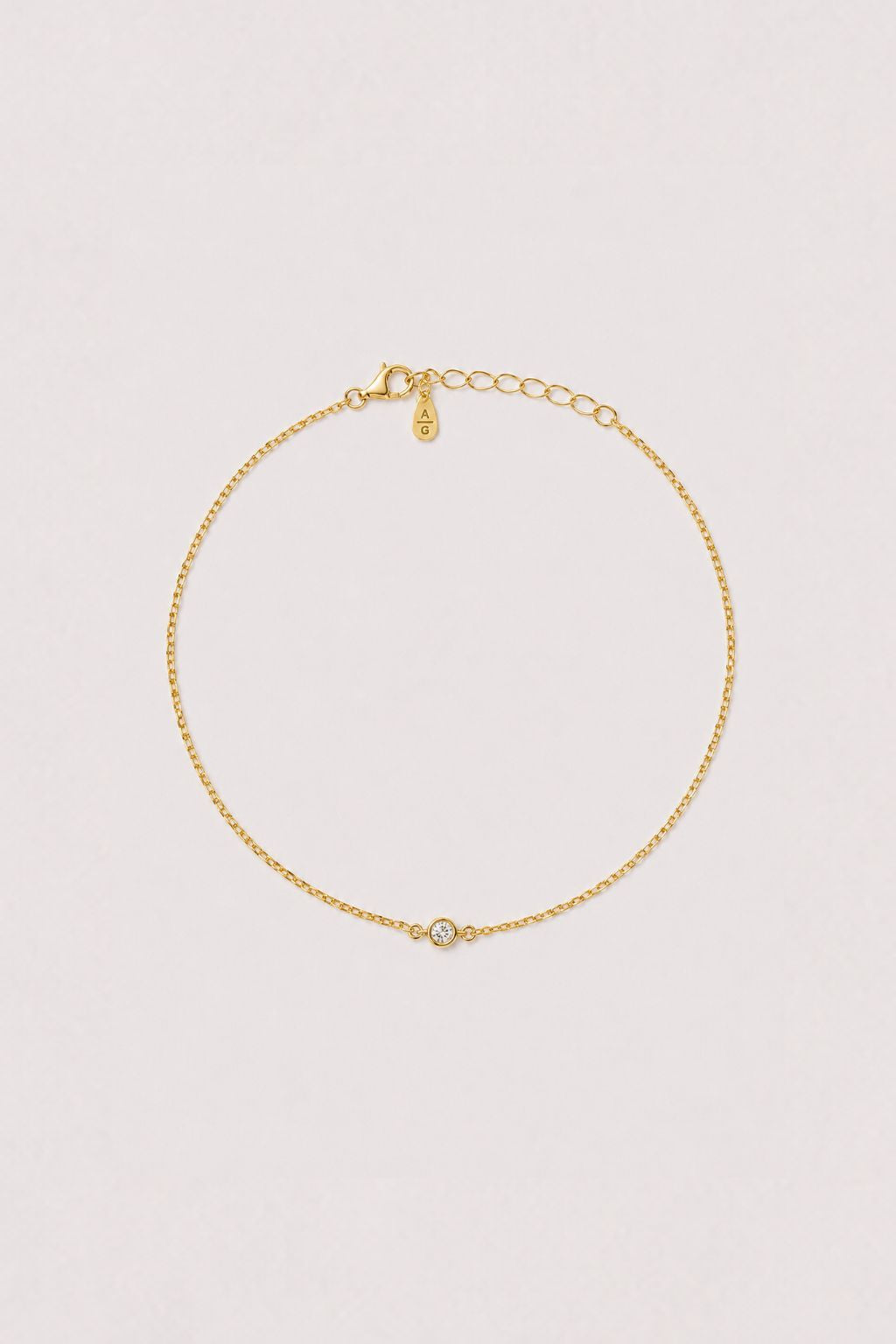 Gold anklet with a small round gemstone on a light gray background