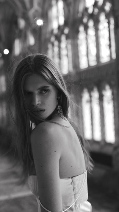 Model in church/dramatic interior, black and white. Long pearl drop bridal earrings editorial — SIENNA by Amélie George