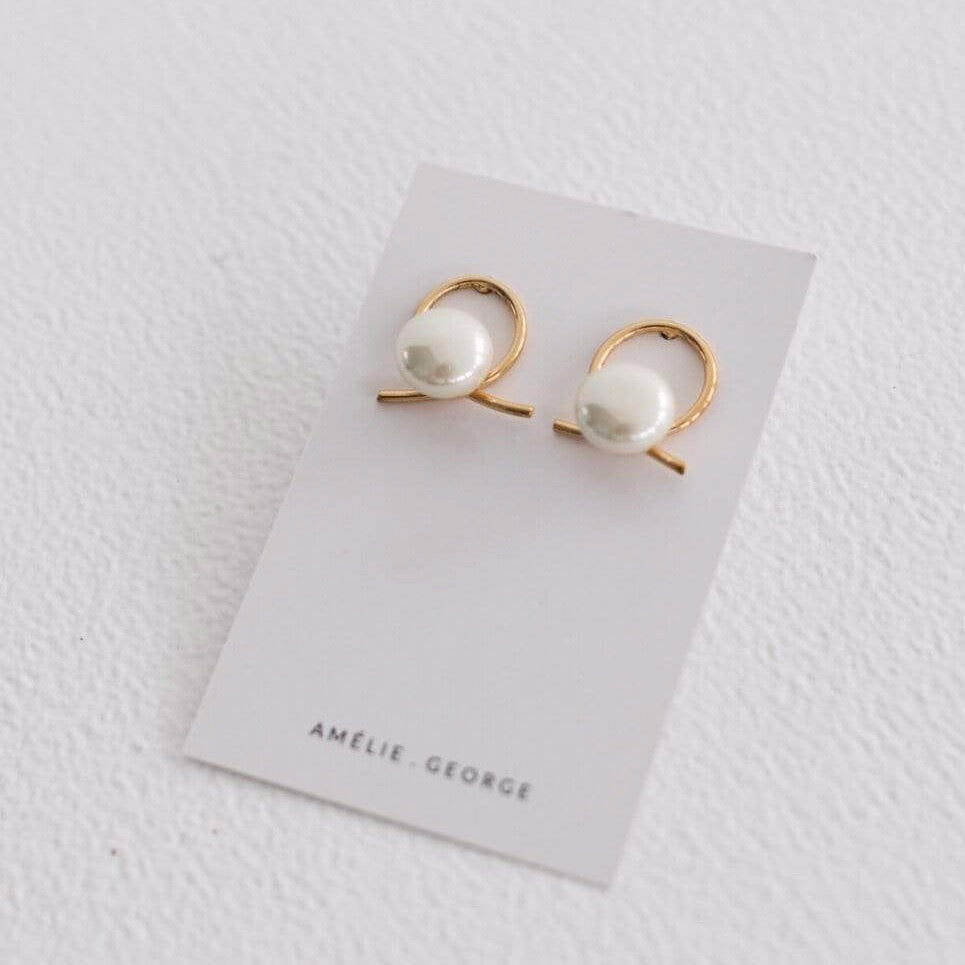 White earring card with a pair of Amelie George Airlie earrings. They have A beige pearl sits in front of a gold ribbon handtwisted into a knot for modern bridal looks
