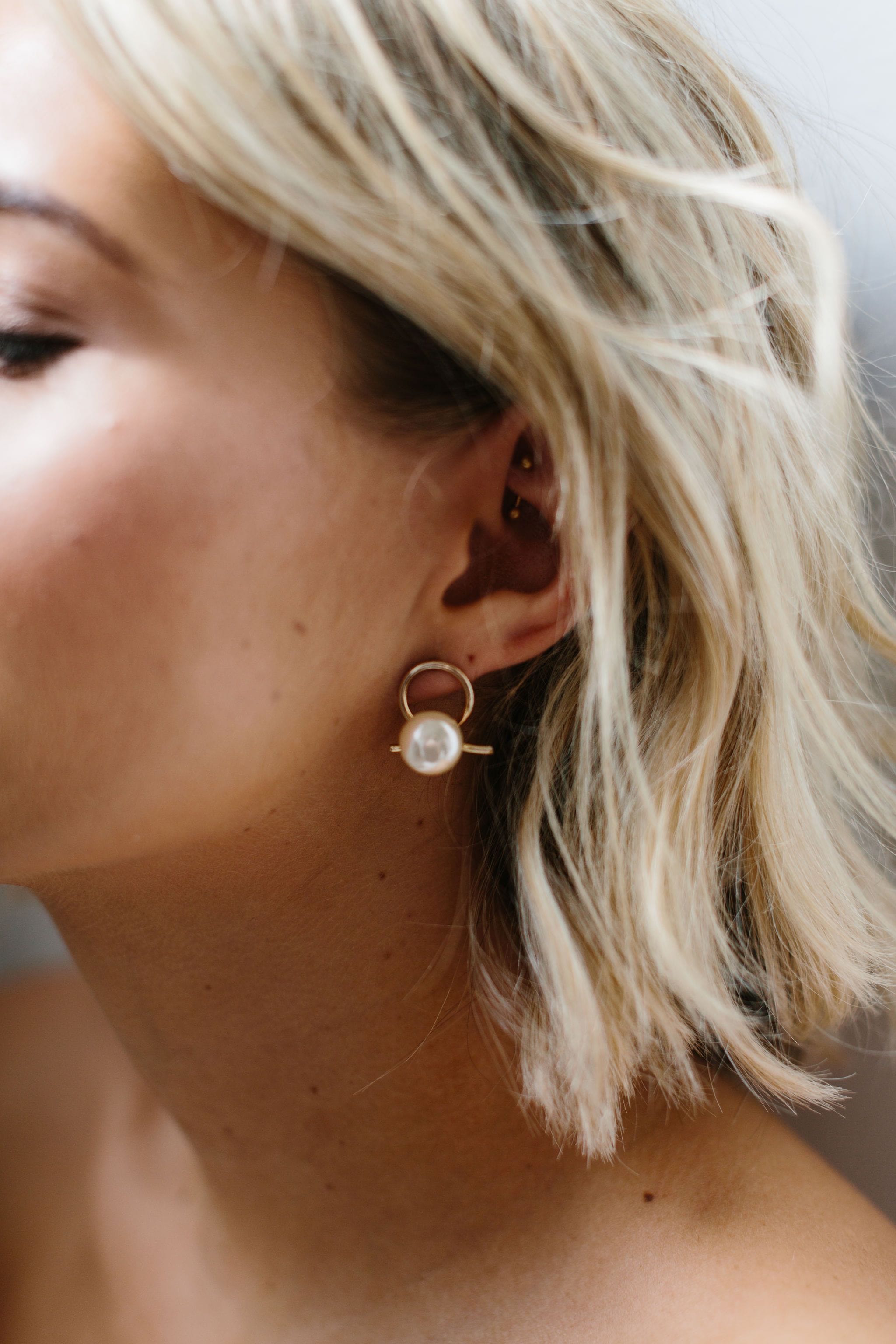 A bride is wearing Amelie George Bridal Airlie Earrings which have a A beige pearl sits in front of a gold ribbon handtwisted into a knot for modern bridal looks