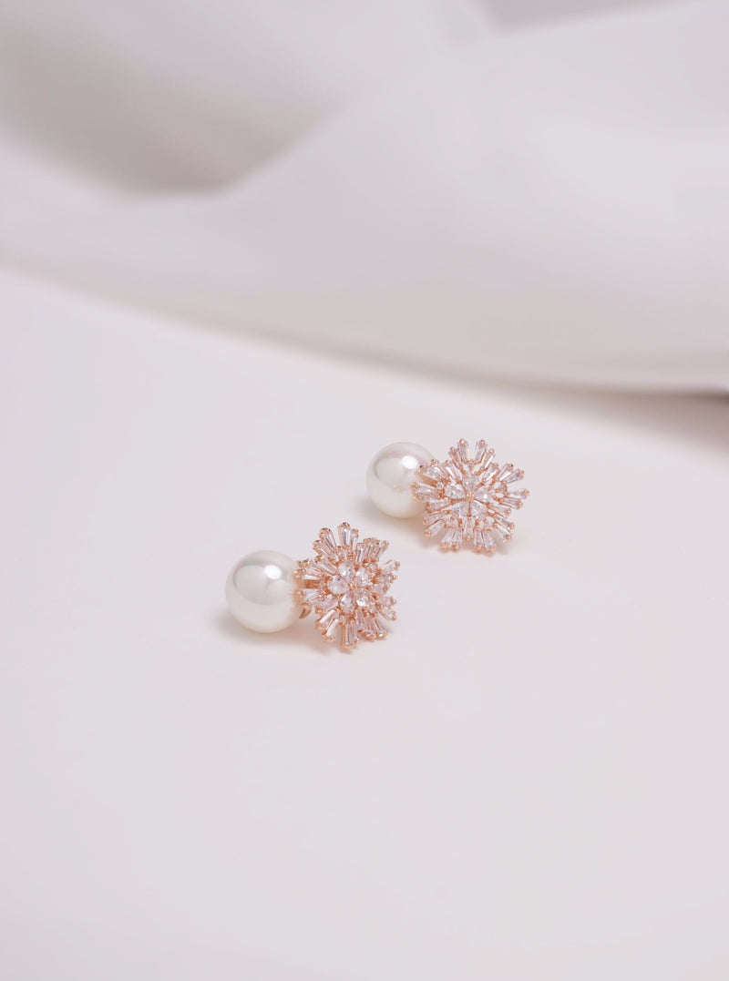 Flatlay of rose gold st clair bridal earrings which have A shimmery handset crystal starburst, gently clasps a pearl dropper for a bold and playful yet refined look.