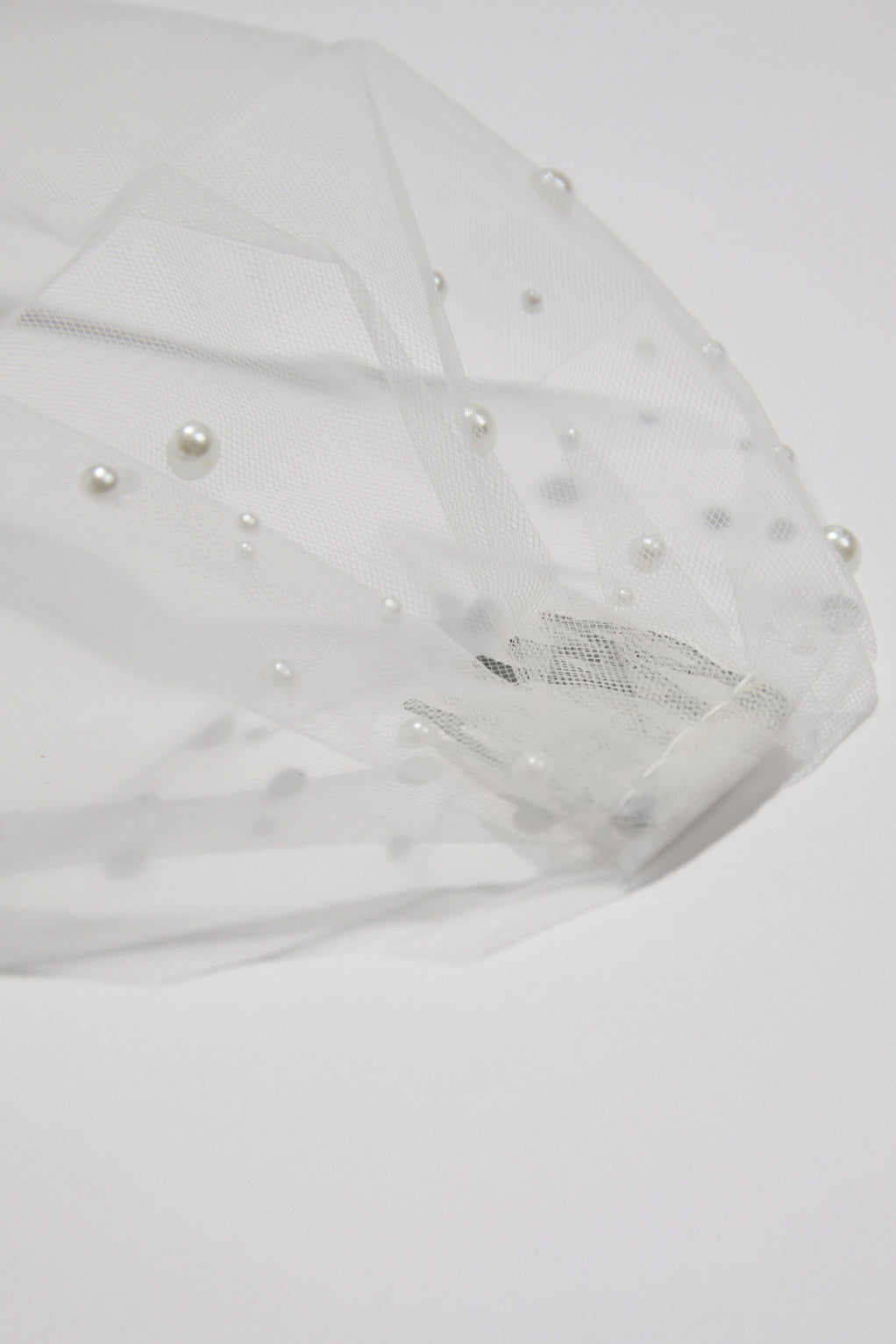Close-up flatlay of a Pearl Birdcage Veil, highlighting the delicate pearls and intricate netting for a luxurious bridal look.