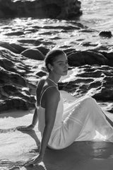 Refined wedding earrings with small pearl and subtle crystal embellishment on a bride sitting on the beach with her hair in a low bun and pearl necklace.